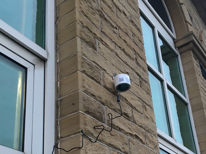A PurpleAir sensor on the wall of a building.