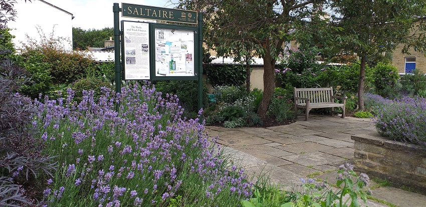 The site of the baths and wash house in Saltaire. There is a notice board, a garden with lavender bushes, and a bench.