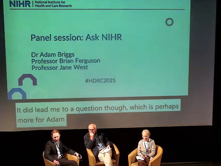 A panel session at the conference. Three people are seated in front of a screen which shows the details of the session, called "Ask NIHR". The panel members are Dr Adam Briggs, Professor Brian Ferguson and Professor Jane West.